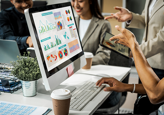 Professionals discussing digital marketing strategies with data charts on a computer screen in an office environment, focusing on restaurant marketing and assisted living facility advertising campaigns.