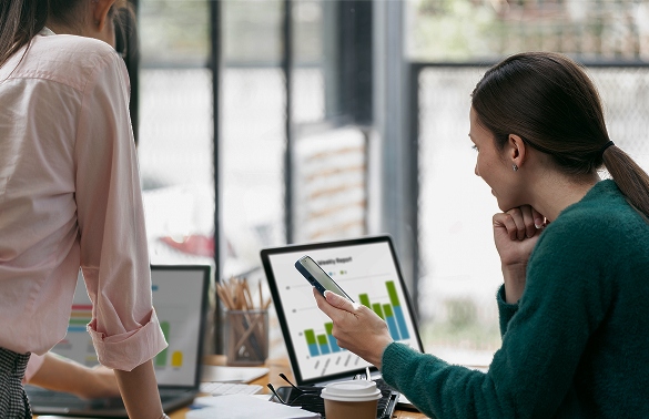 Two people in a meeting analyzing marketing data on laptops, focusing on graphs and statistics, emphasizing digital marketing strategies for restaurants and assisted living facilities. Coffee cup on the table adds a casual office environment vibe.