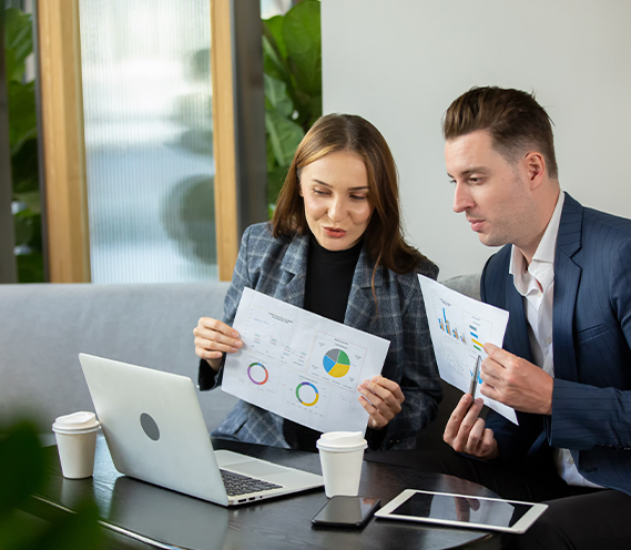 Two business professionals analyzing charts on paper while sitting with a laptop in an office setting. Digital marketing strategy discussion.