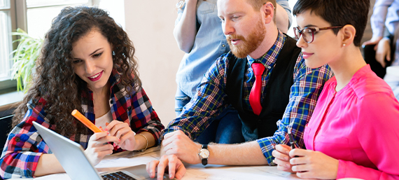 Young professionals collaborating at a laptop, discussing digital marketing strategies for restaurants and assisted living facilities.